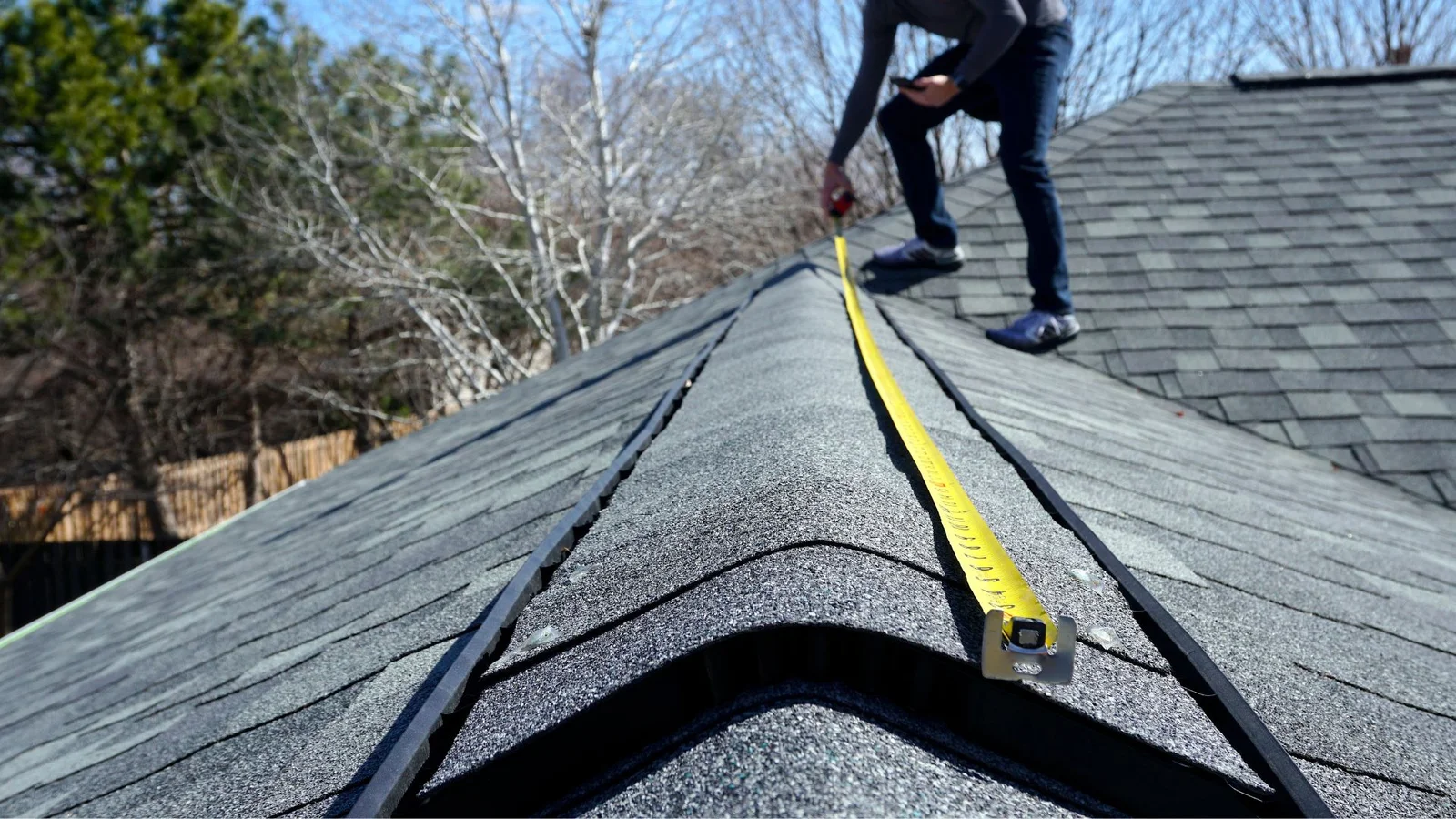 Roof inspector measuring asphalt shingle roof with ridge vent and metal flashing details