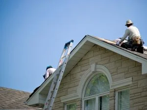 Roofing contractors inspecting pitched residential roof with architectural shingles