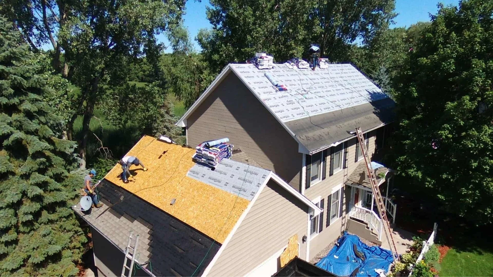 Roof replacement in progress showing yellow OSB sheathing, underlayment, and new shingles on multi-pitched residential roof