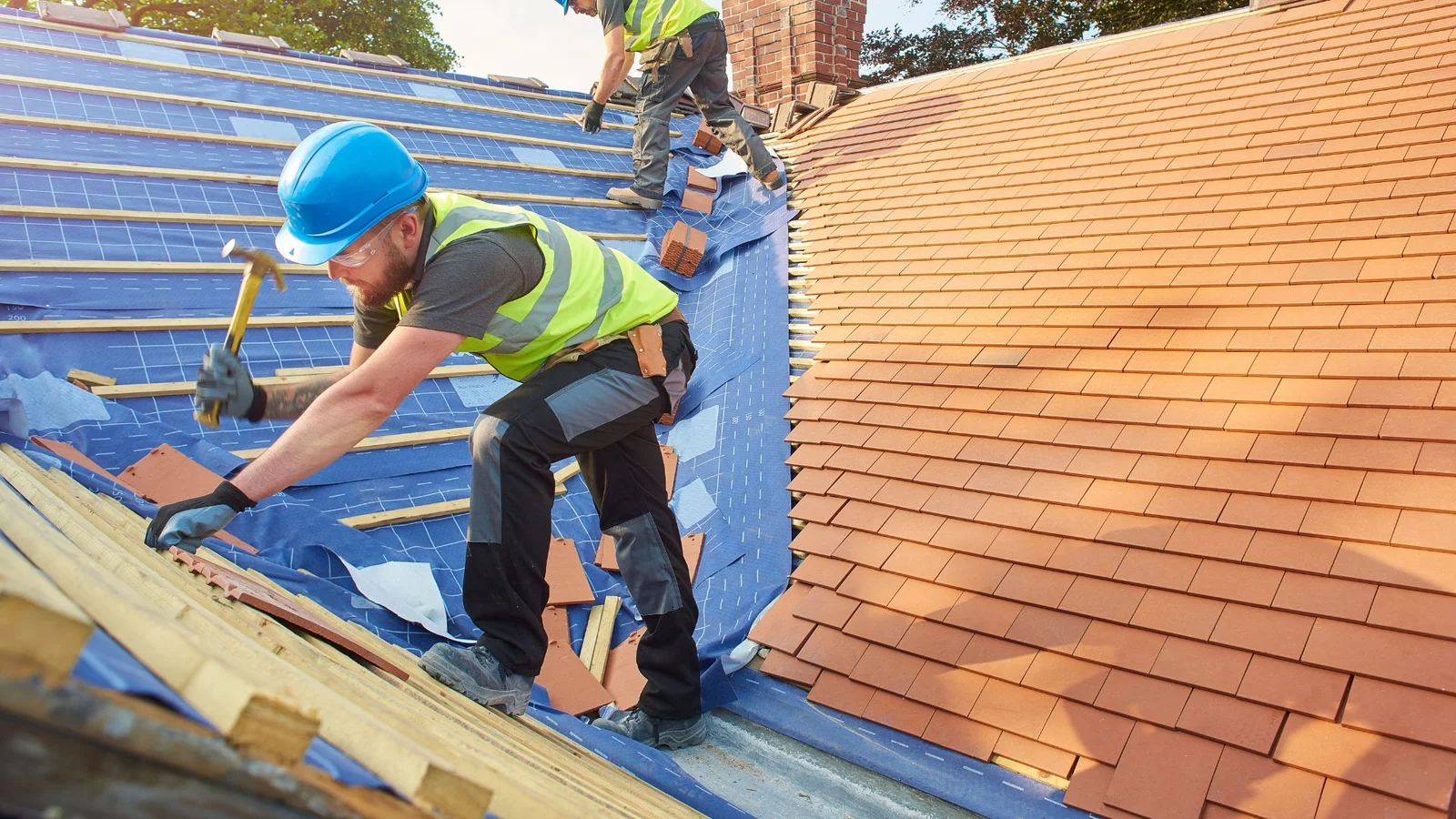 Roofers installing clay tile shingles over blue underlayment on pitched roof