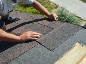 Worker installing asphalt shingles on roof deck with proper overlap and alignment