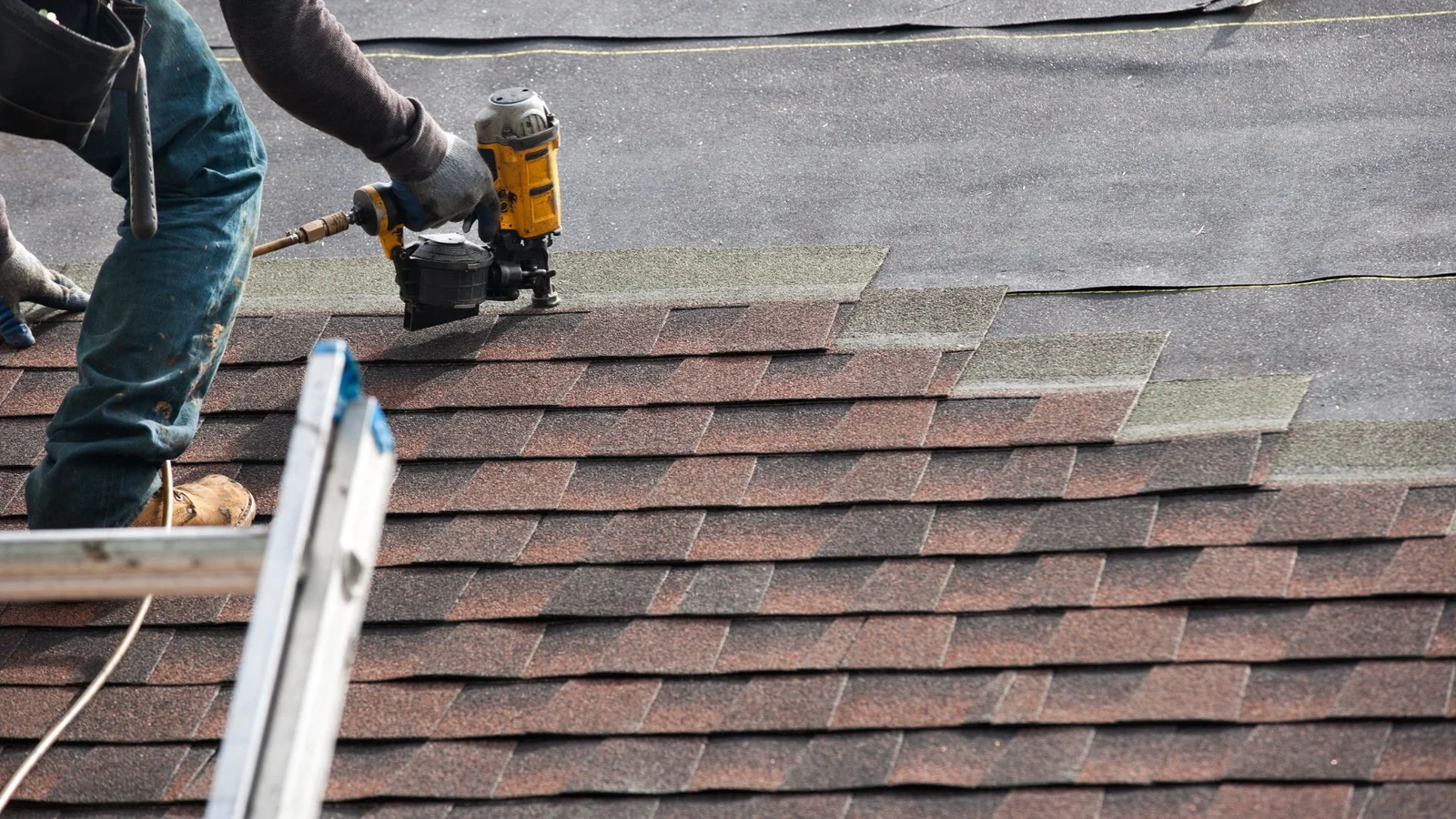 Roofer installing asphalt shingles with pneumatic nailer on residential roof