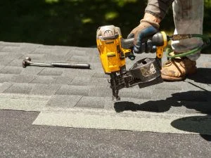 Roofer using pneumatic nailer to install asphalt shingles on roof deck
